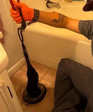A technician pulling a hair and debris clog out of a bathtub drain in a Flagstaff home