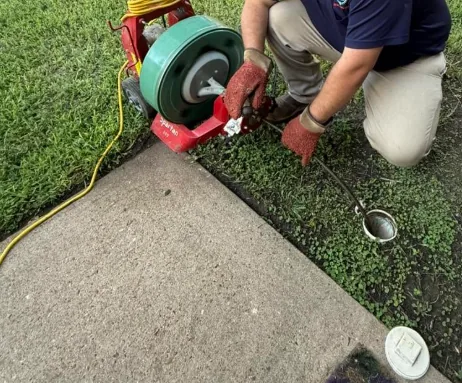 Drain cleaning technician feeding a cable machine into a sewer cleanout in a Flagstaff yard