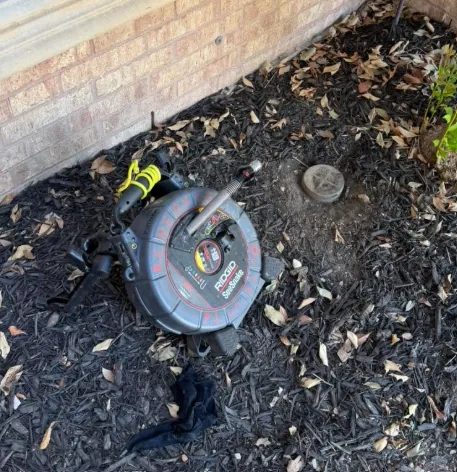 Sewer camera reel set beside a brick home cleanout