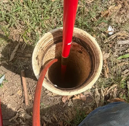 Red jetting hose running down into an exposed sewer cleanout pipe