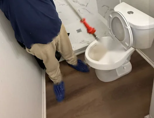 Technician running a drain auger into a toilet to clear a clog